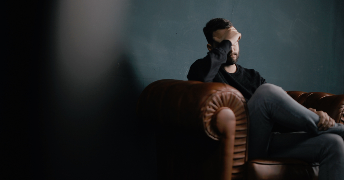 man sitting on couch with his head in his hands